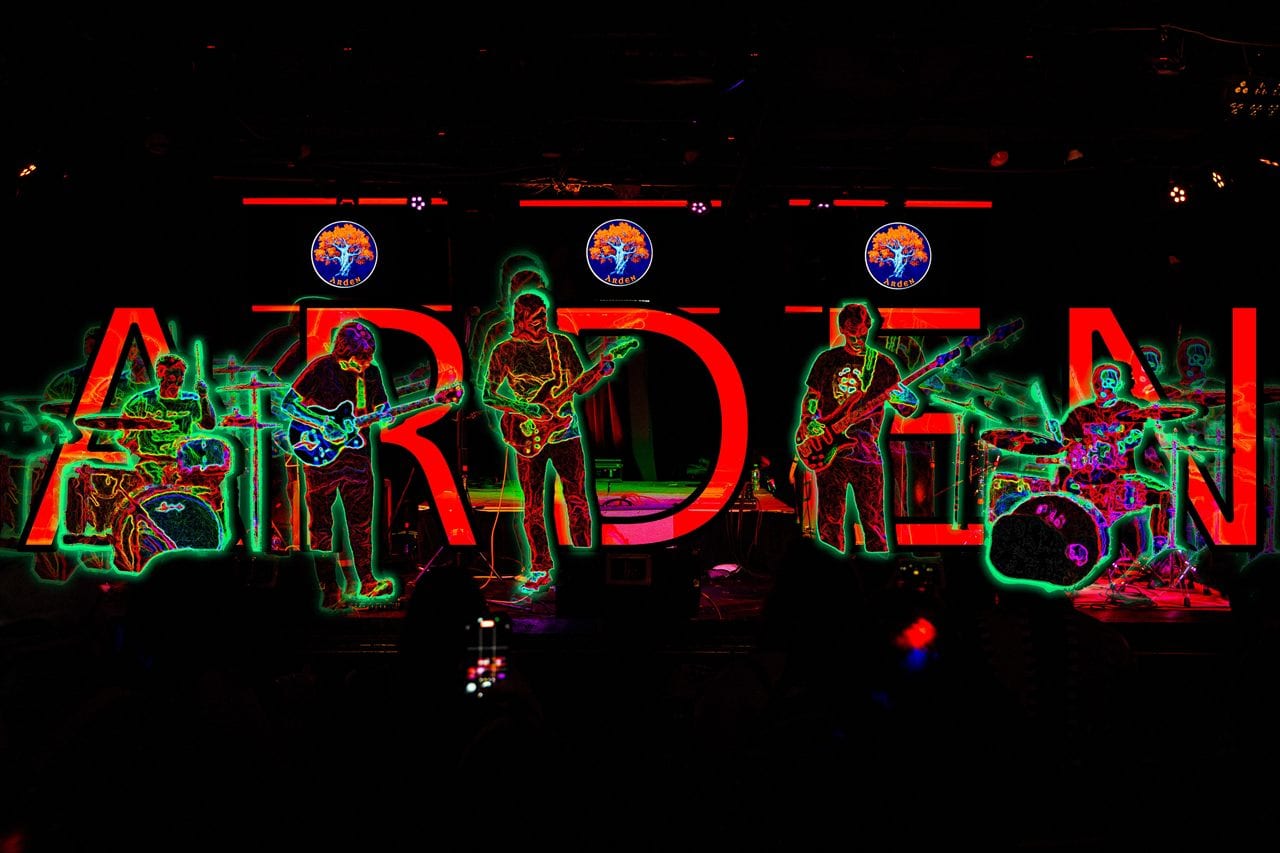 Arden performing live — the band on stage under neon ARDEN lettering
